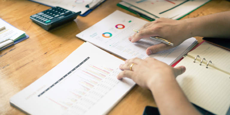 Top view of a financial planner’s desk with financial planning documents and a calculator on it, and his hands on the desk.